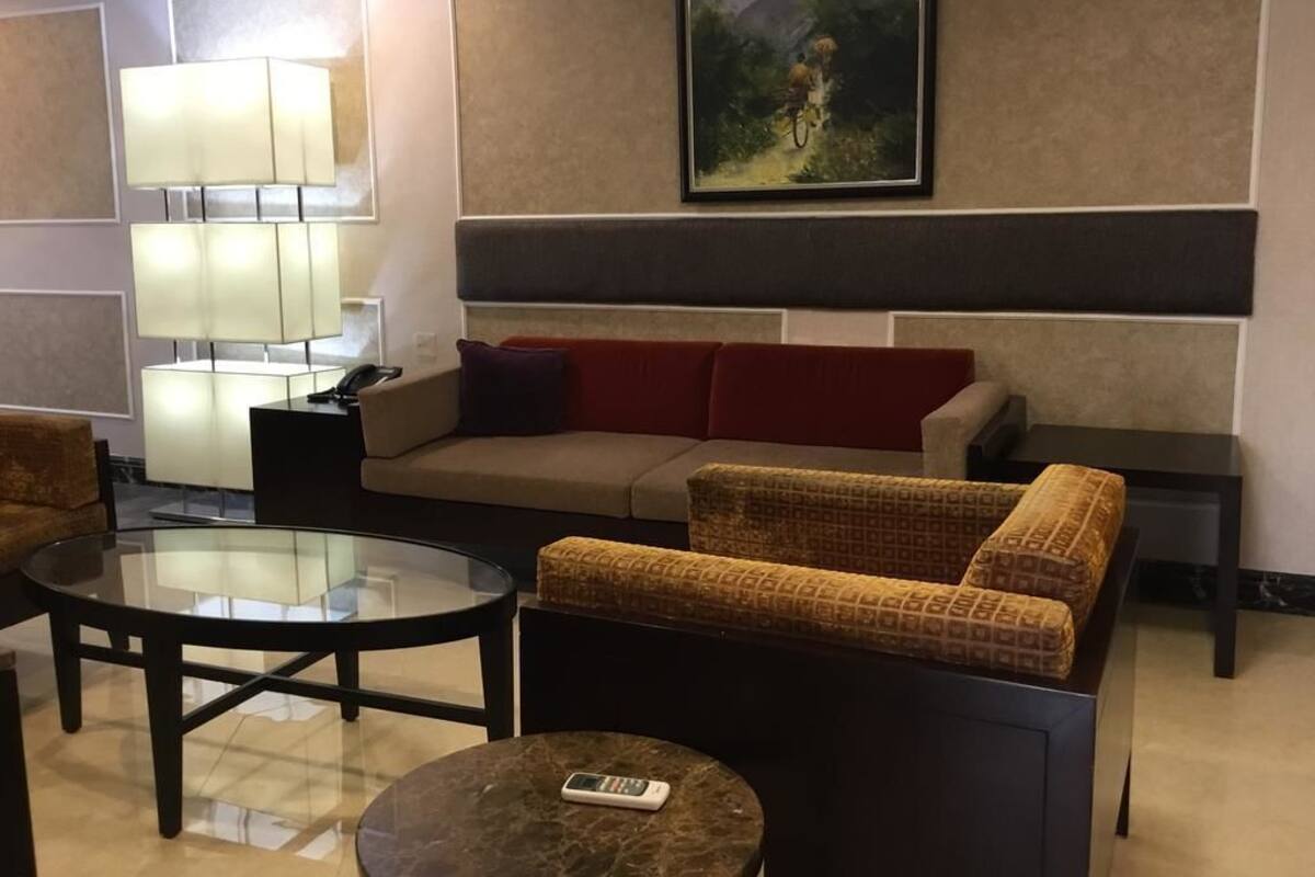 A hotel room with a sofa, a glass coffee table, a lamp, and a painting on the wall.