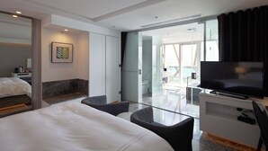 A modern hotel room with a bed, a TV, a desk, and a glass door leading to a balcony. - Volando Kenting (Hengchun)