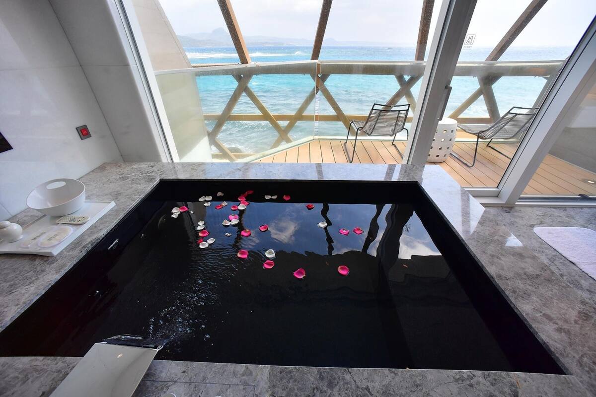 A spa area with a large black bathtub, a wooden deck, and a view of the ocean.