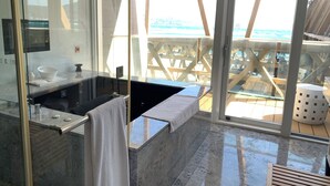 A modern bathroom with a large bathtub, a glass shower enclosure, and a view of the beach through large windows. - Volando Kenting (Hengchun)