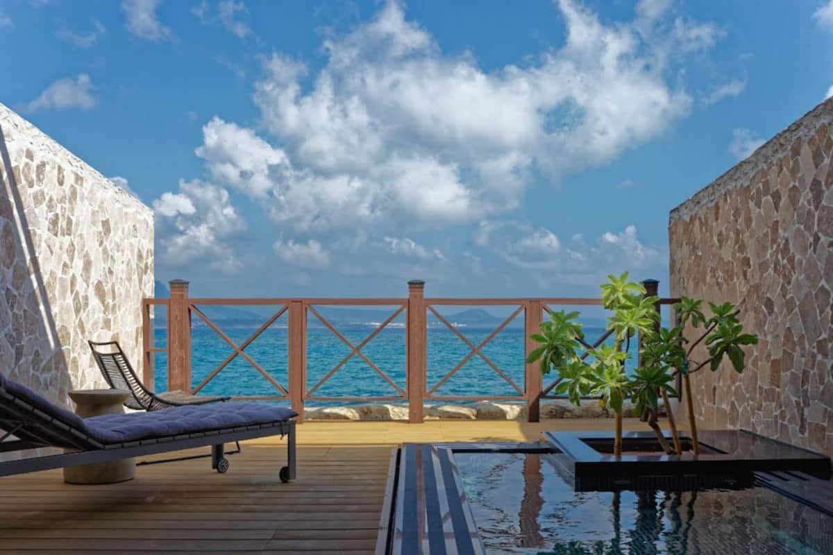 A wooden deck with a pool, lounge chairs, and a view of the ocean.
