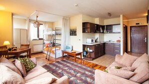 Ett kompakt bostadsutrymme med ett litet kök, en matplats med bord och stolar samt en sittgrupp med soffor.