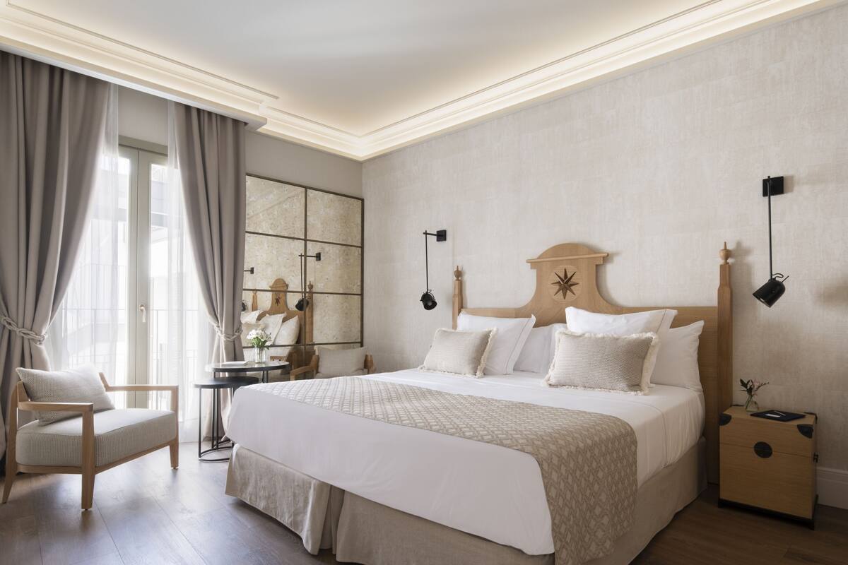 A neatly arranged bedroom with a large bed, a bedside table, a chair, and a small desk.