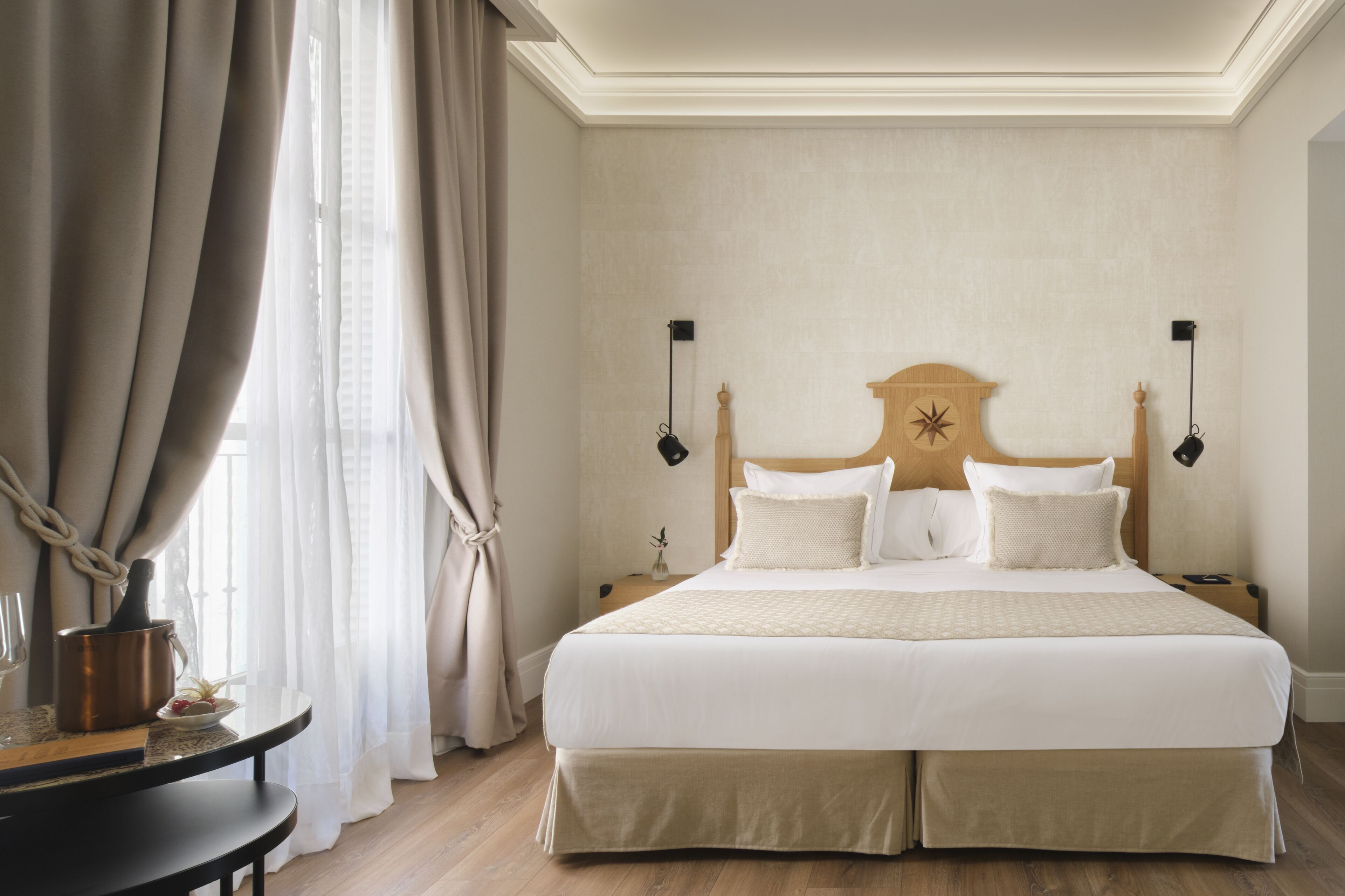 Una cama bien hecha con cabecera de madera, dos lámparas de noche y una mesita de noche con lámpara y un pequeño jarrón.