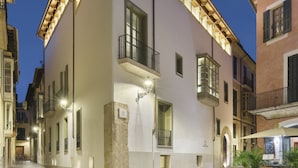 Un edificio histórico con base de piedra, techo plano y balcón con barandilla de metal.