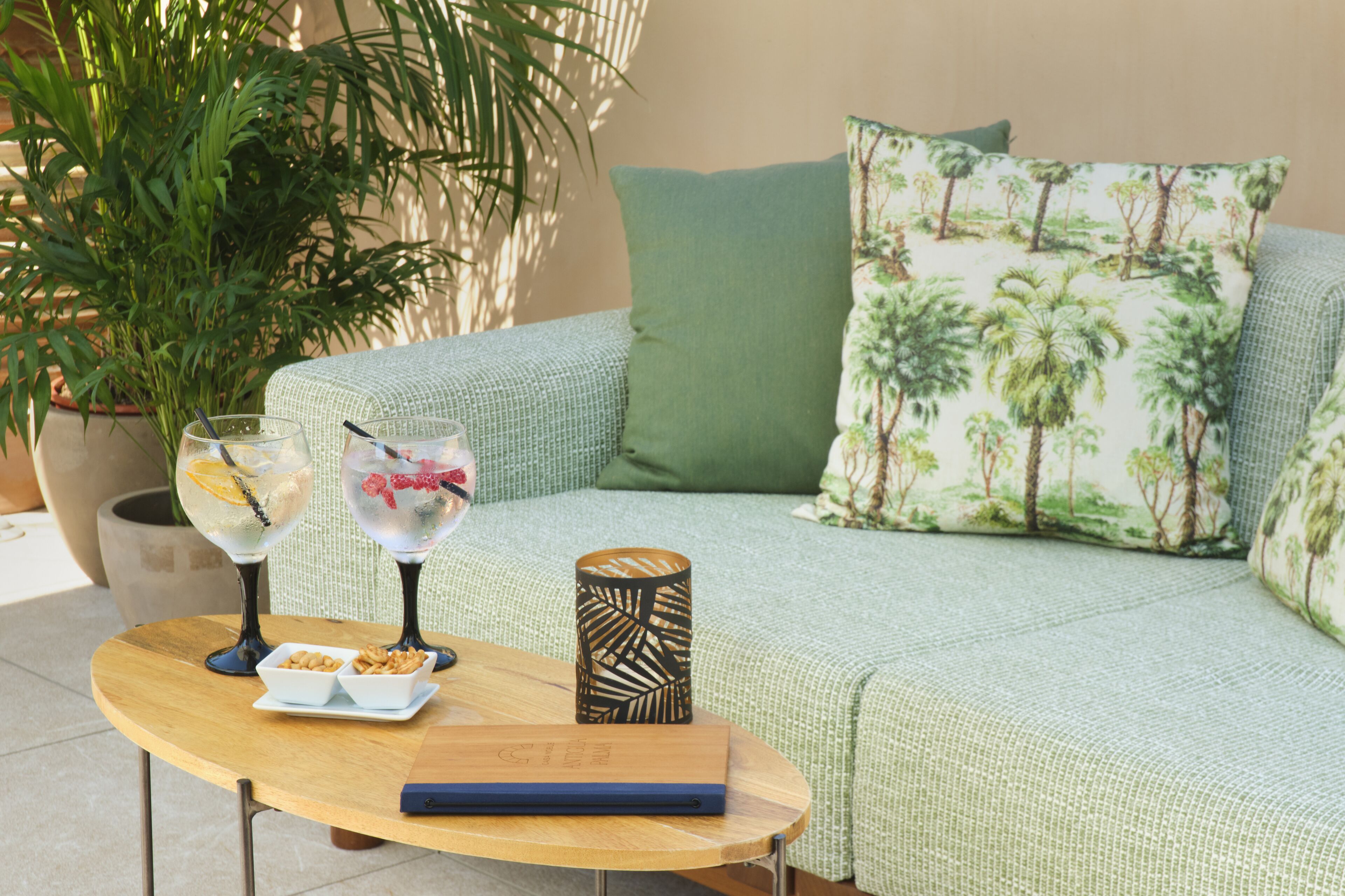 Un espace extérieur accueillant avec un canapé confortable, une petite table avec des collations, deux verres d’eau et une bougie décorative.