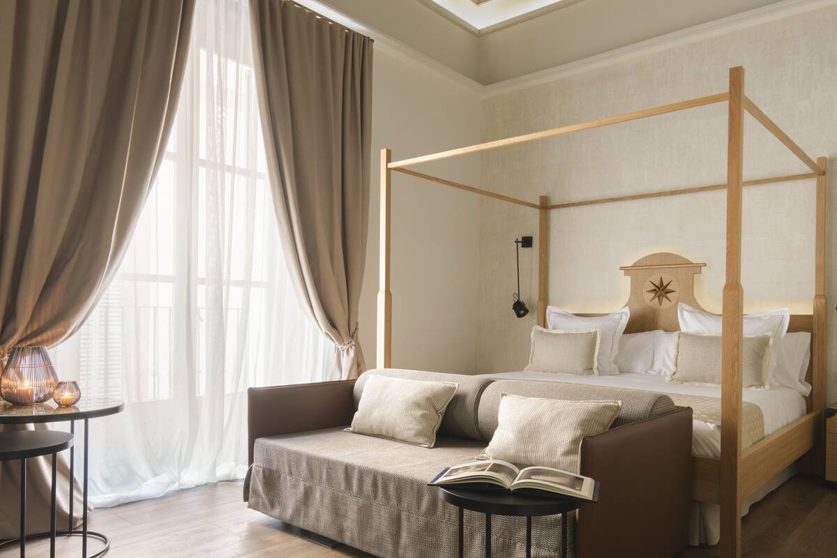 A four-poster bed with a canopy, a sofa, a small round table, and a large window with curtains.