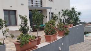 A modern building with a balcony, potted plants, and a view of the sea. - Villa with private pool, sicily, Palermo. (Trabia)