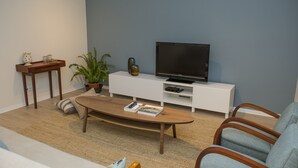 Ein Wohnzimmer mit einem Holztisch, einer weißen Unterhaltungsecke, einem Fernseher und einer Topfpflanze.