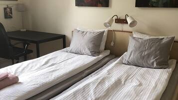 Een hotelkamer met twee eenpersoonsbedden, een bureau, een stoel en twee wandlampen.