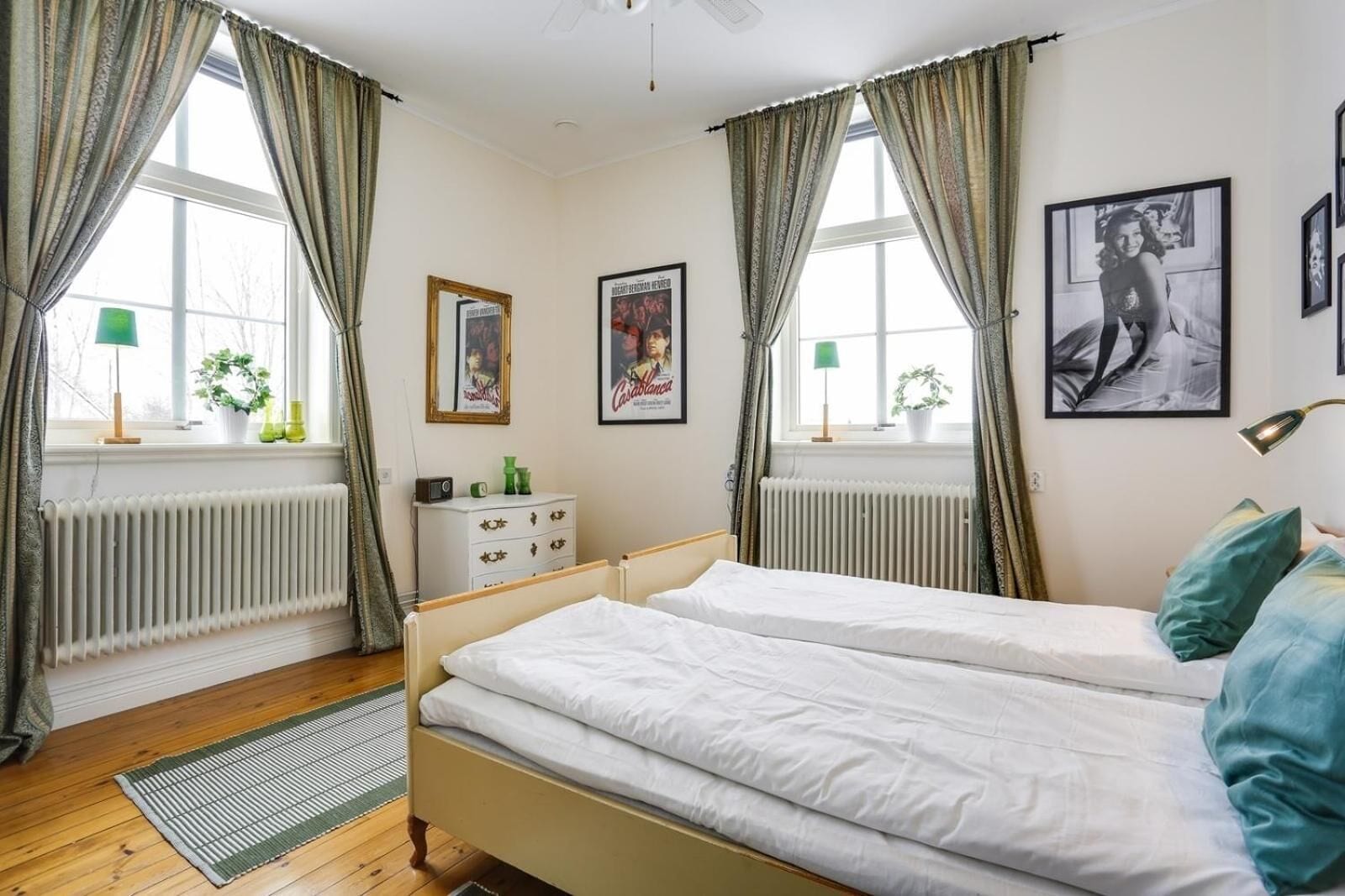Une chambre avec deux lits, une commode, un radiateur et des tableaux encadrés accrochés au mur.