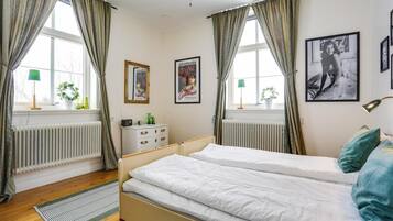 Une chambre avec deux lits, une commode, un radiateur et des tableaux encadrés accrochés au mur.