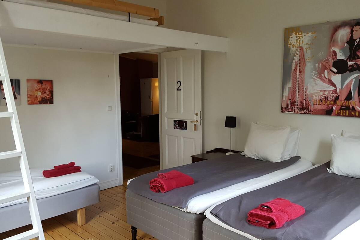 A room with two beds, a ladder, a door, and a poster on the wall.