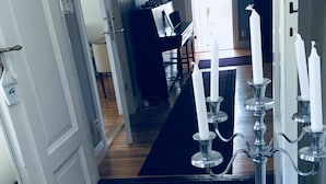 A hallway with a wooden floor leading to a room with a black rug. A candelabra with white candles is visible in the foreground. - Hagbackens GĂ„rd Bed & Breakfast (Ărebro)