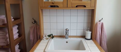 Un baño con un lavamanos blanco, armarios de madera y un perchero para toallas.