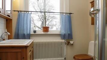 Un bany amb un tocador de fusta, un vàter blanc, una finestra amb cortines blaves i un radiador.