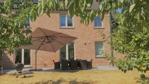 Un bâtiment en briques doté d’un patio comprenant un barbecue, du mobilier d’extérieur et un grand parasol.