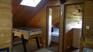 Un pequeño cuarto en el ático con techo inclinado de madera, una mesa de fútbol de mesa, una cama y una puerta que da a otra habitación.