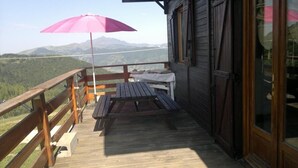 Una terraza de madera con una mesa, bancos, un paraguas rosa y vistas a las montañas.