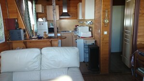 Habitación compacta con kitchenette, un refrigerador pequeño, microondas y lavamanos. Hay un sofá blanco y una puerta de madera.