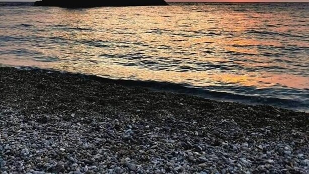 A sunset over a calm sea with a rocky outcrop silhouetted against the sky. - Campo Sportivo (Taurianova)