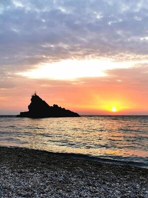 A sunset over a calm sea with a rocky outcrop silhouetted against the sky. - Campo Sportivo (Taurianova)