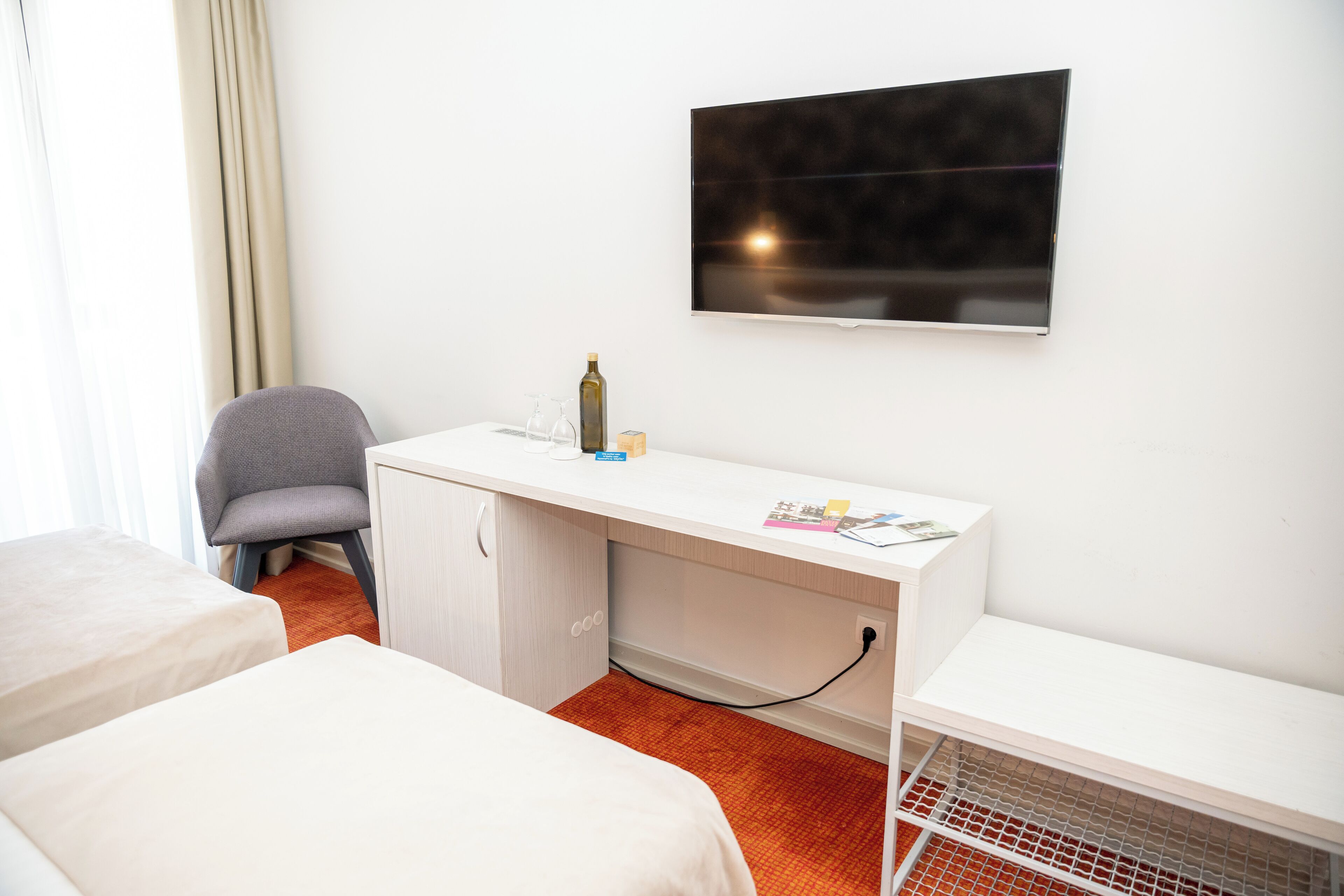 A hotel room with a bed, a desk, a chair, a TV, and a minibar.