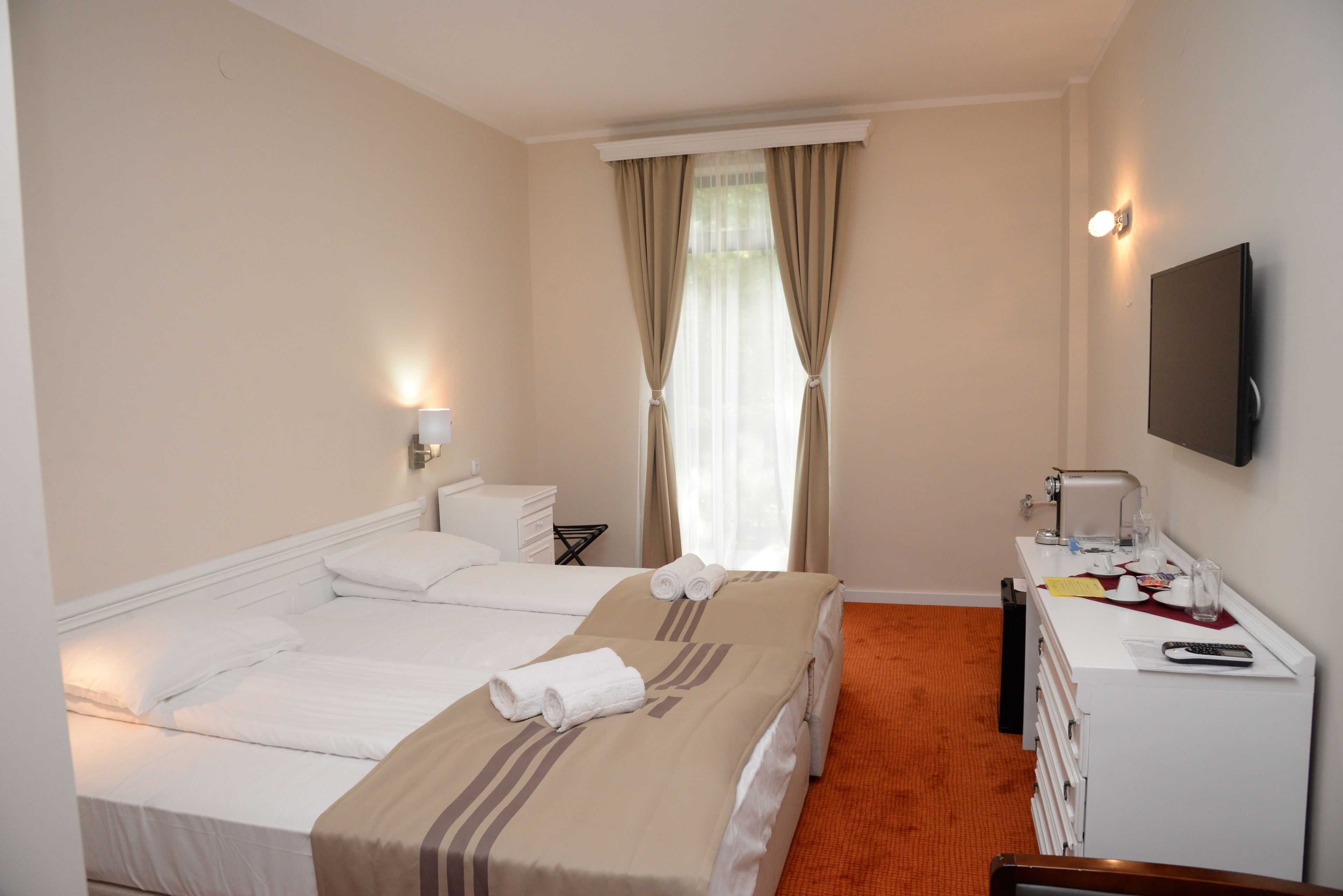 Une chambre d’hôtel avec deux lits, un bureau avec une lampe, une télévision et une fenêtre avec des rideaux.