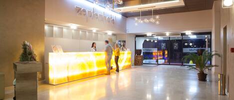 A hotel reception area with a bright, illuminated desk and a sign reading "zephyr hotel".
