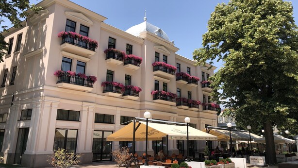 Ett hotell med flera balkonger som är dekorerade med rosa blommor, utomhusområden med sittplatser och en stor, central kupol.