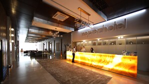 En hotellobby med modern design, som inkluderar en receptionsdisk, en stor, upplyst informationsskärm och en rymlig entréhall.
