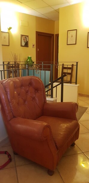 A brown leather armchair in a hallway with yellow walls, a wooden door, and a blue railing. - Masseria Frangiosa (Torrecuso)