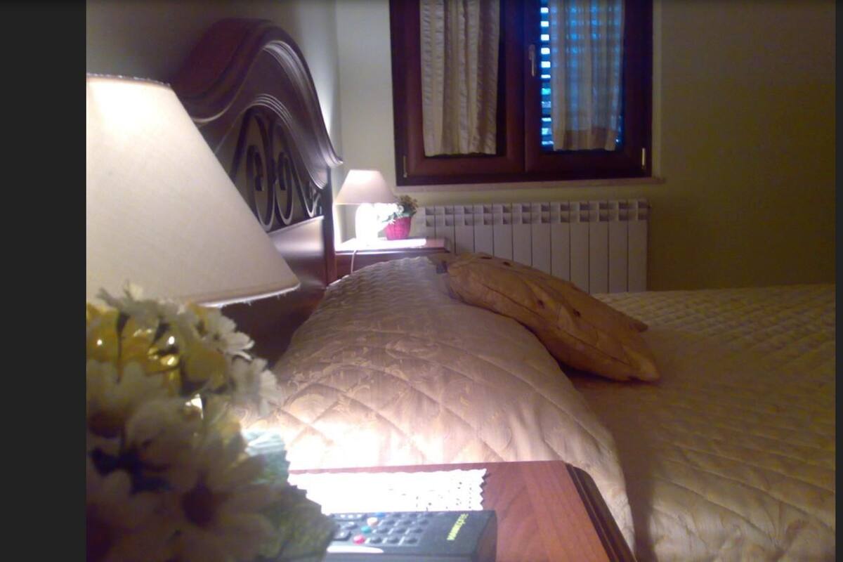 A bedroom with a bed, a nightstand, a lamp, and a window with curtains.