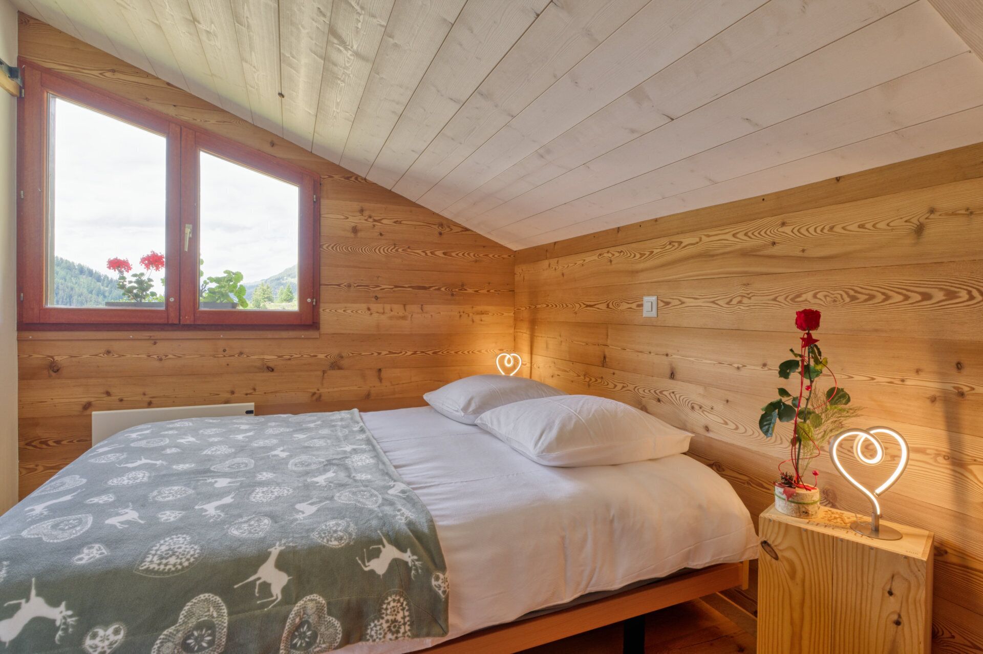 Een houten slaapkamer met een bed, een raam en een nachtkastje met een bloem.