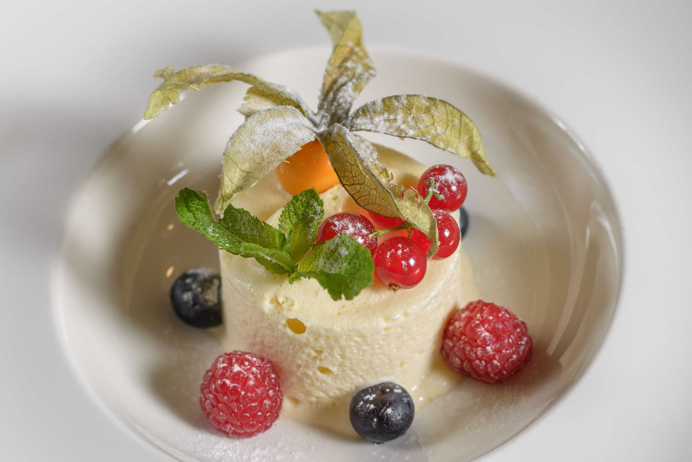 Un postre con frutos rojos y hojas de menta sobre un plato blanco.