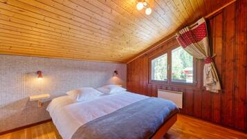 A wooden-paneled bedroom with a bed, two wall-mounted lights, a window with curtains, and a radiator.