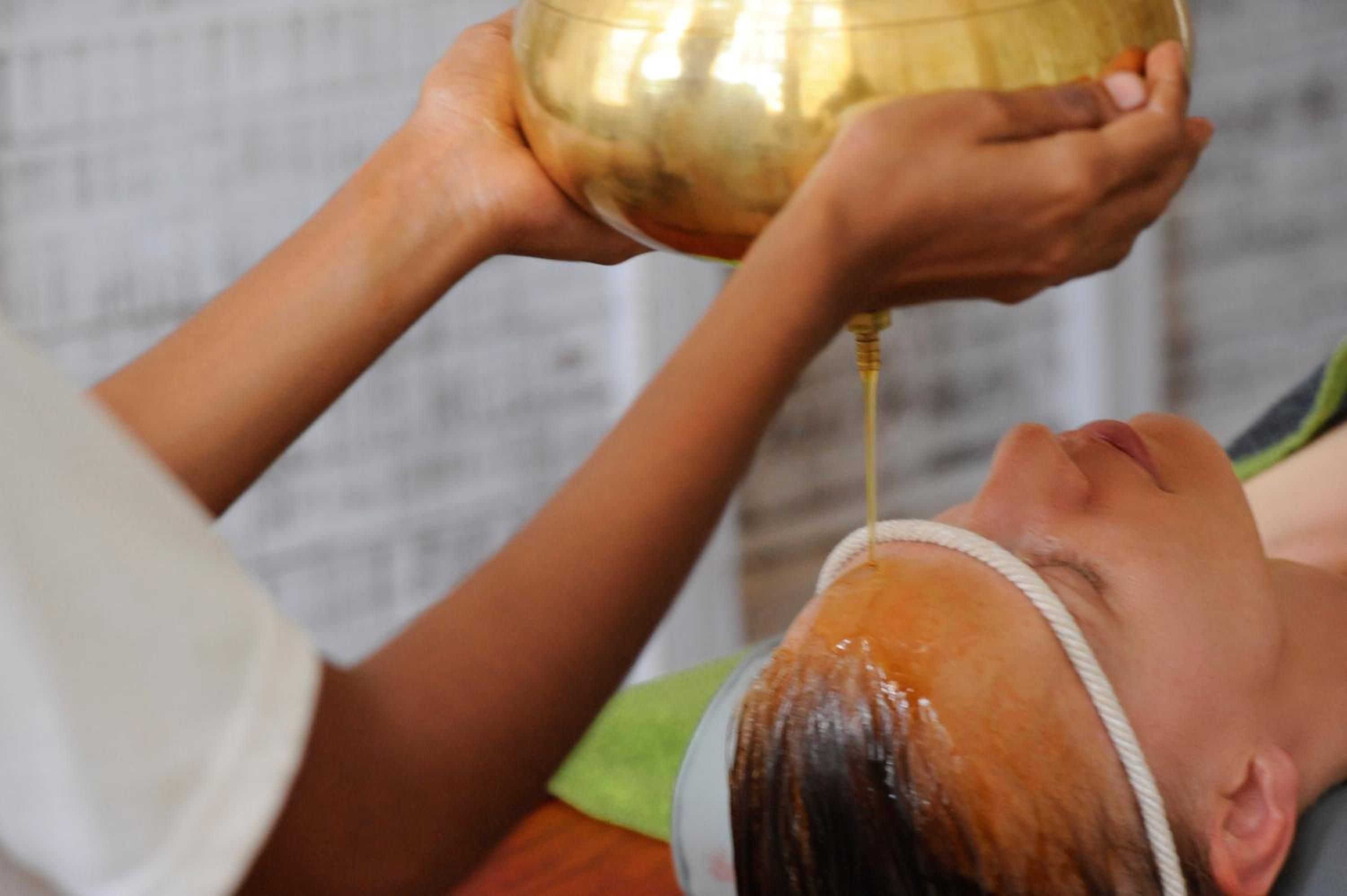 A person receiving a treatment with a golden bowl.