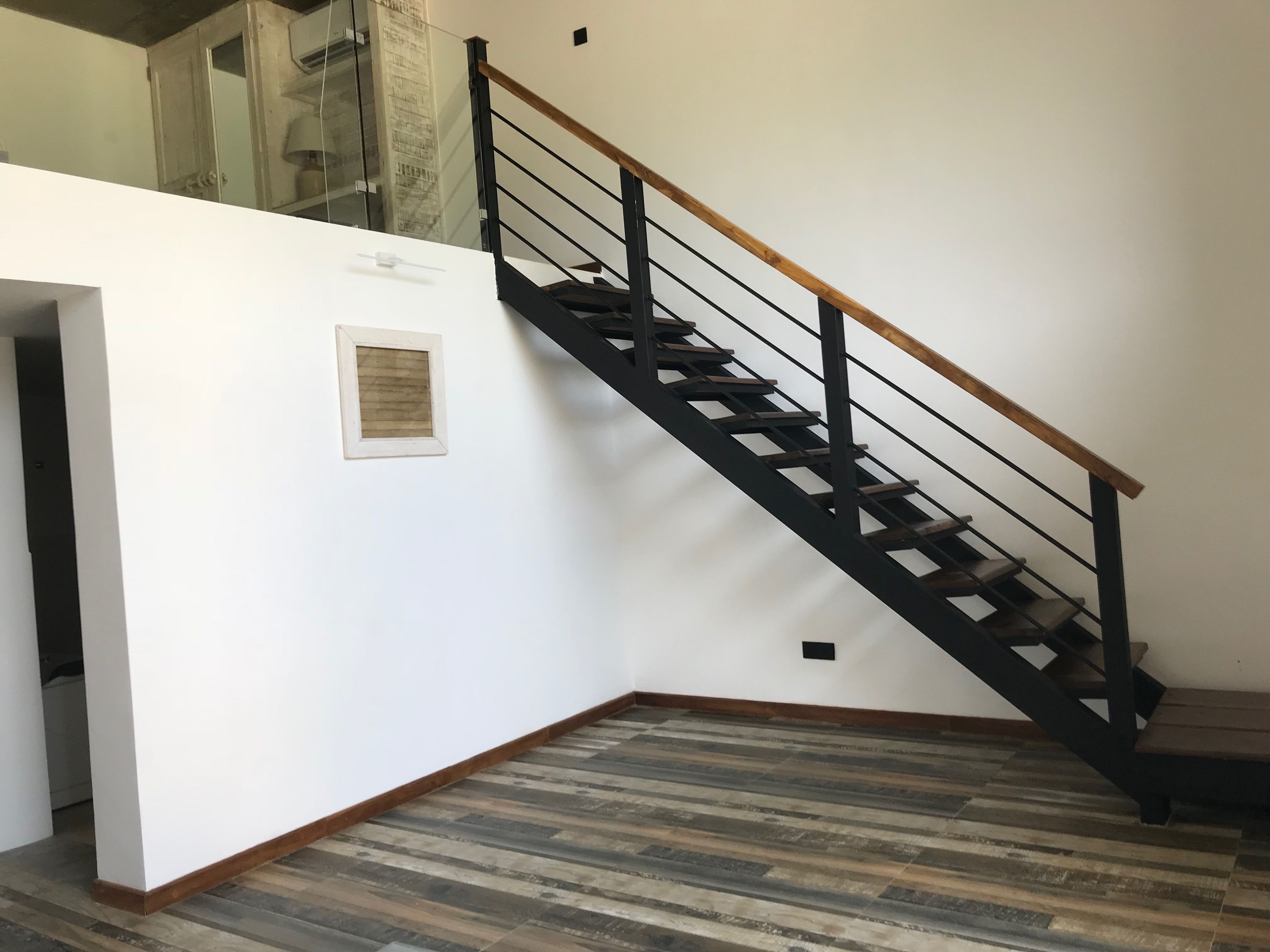 Un escalier avec une main courante en bois et des balustrades en métal noir, menant à l’étage supérieur.
