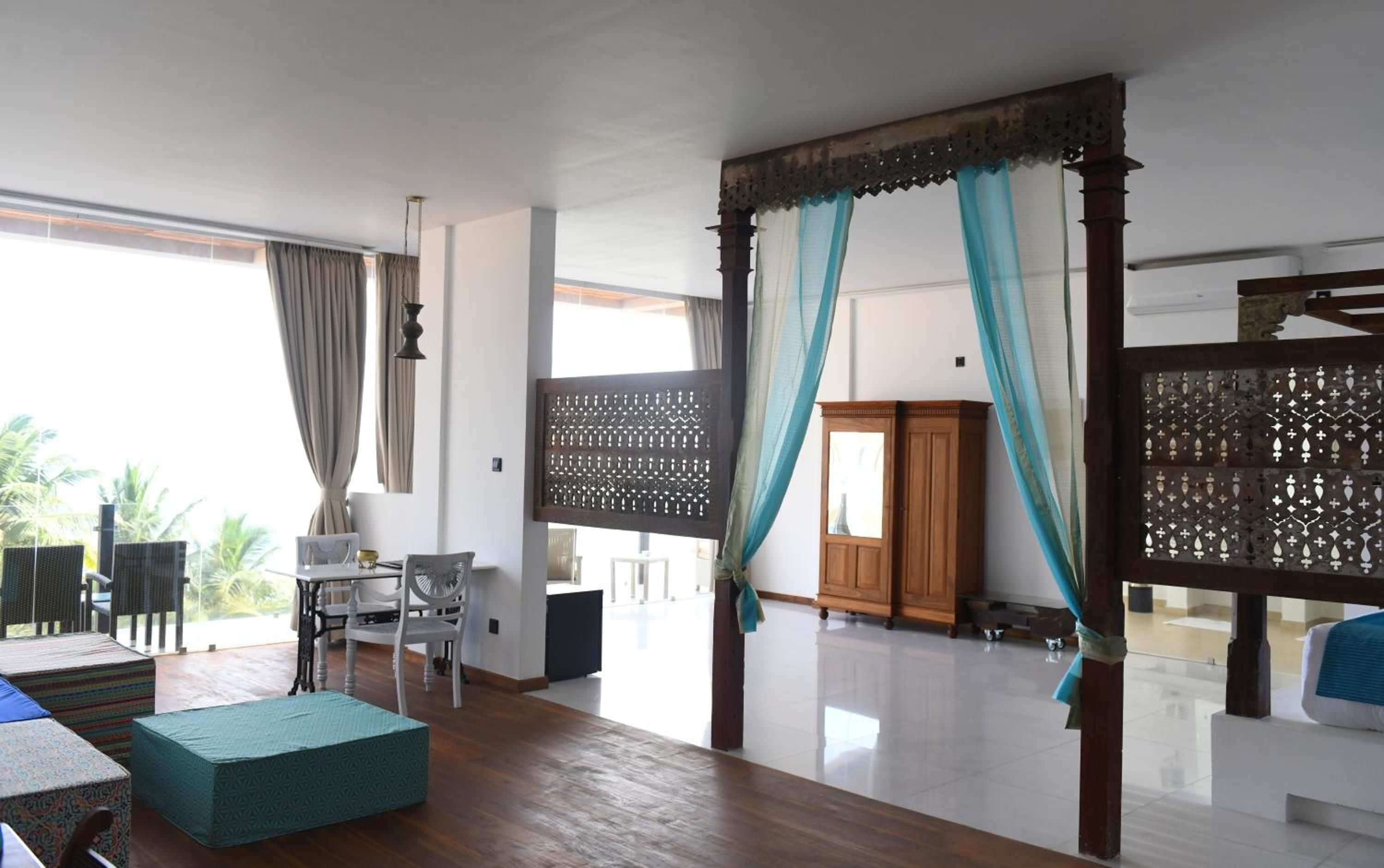 A spacious room with a large window, a wooden floor, a seating area with a table and chairs, and a decorative screen.
