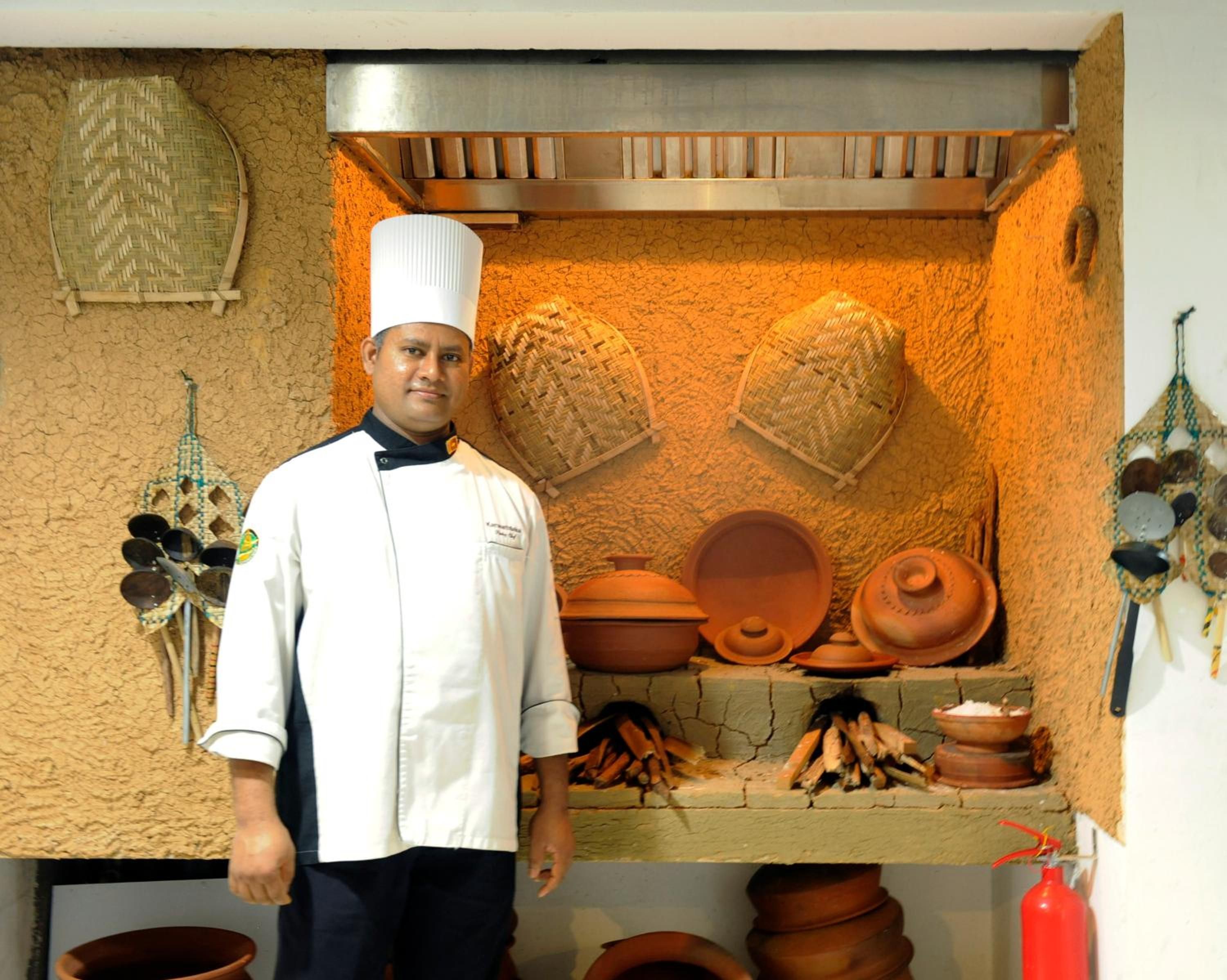 A chef standing in a kitchen with traditional cookware and utensils.