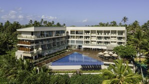 Ein modernes Hotel mit einem zentral gelegenen Schwimmbecken, umgeben von üppiger Vegetation und Palmen.