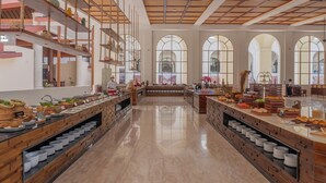 A spacious buffet area with multiple serving counters, a high ceiling with a grid pattern, and large arched windows allowing natural light. - NDC Resort (Manado)