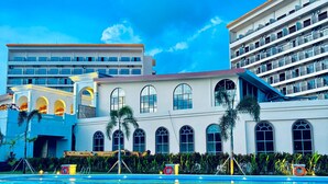 A hotel with a swimming pool, multiple balconies, and a clear blue sky. - NDC Resort (Manado)