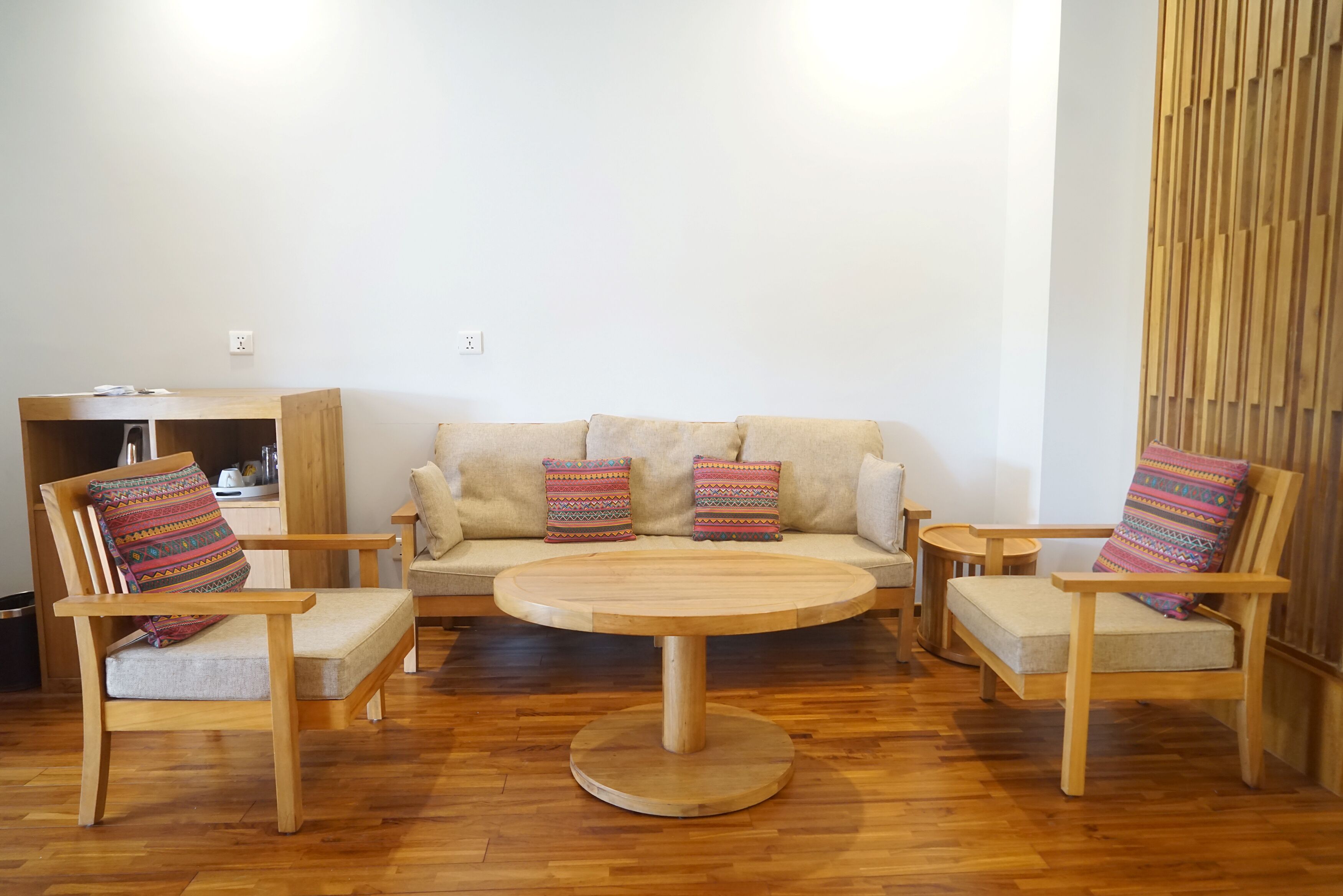 Una sala de estar con una mesa de centro de madera, dos sillones, un sofá y cojines coloridos.