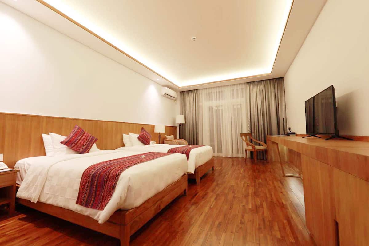 A hotel room with two beds, a desk, a chair, a television, and a window with curtains.
