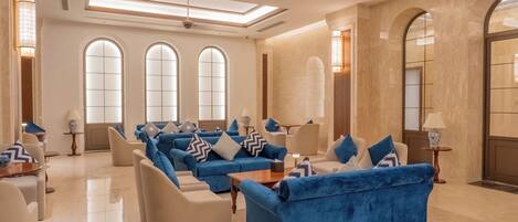 A spacious living area with blue sofas, beige armchairs, and a central coffee table.
