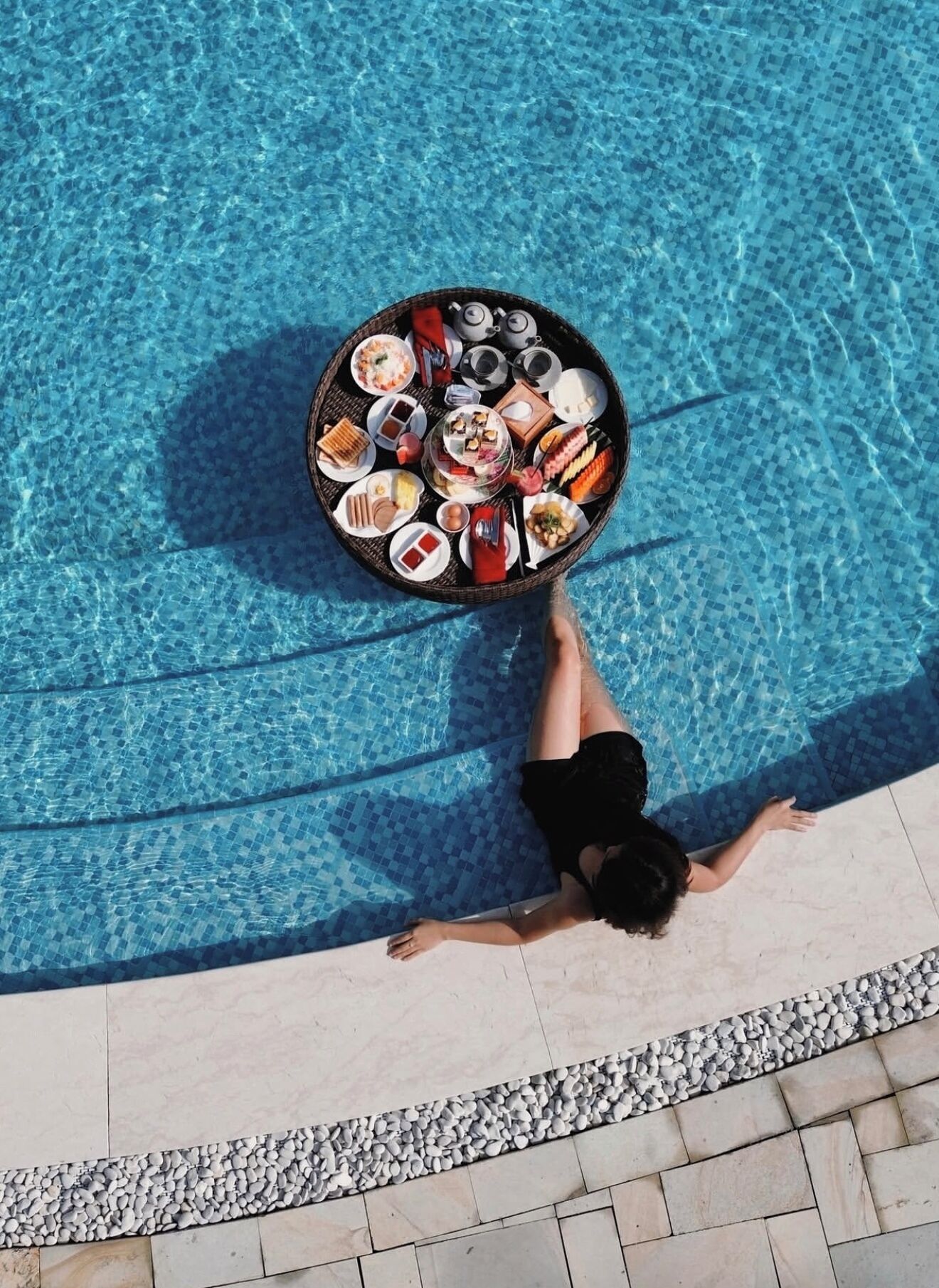 A person relaxing by a pool with a tray of food.