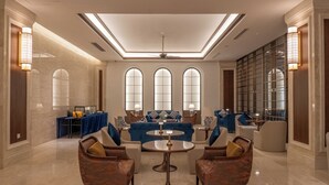 A spacious lobby with a high ceiling, a central seating area with sofas and armchairs, a dining table, and a large window with multiple panes. - NDC Resort (Manado)