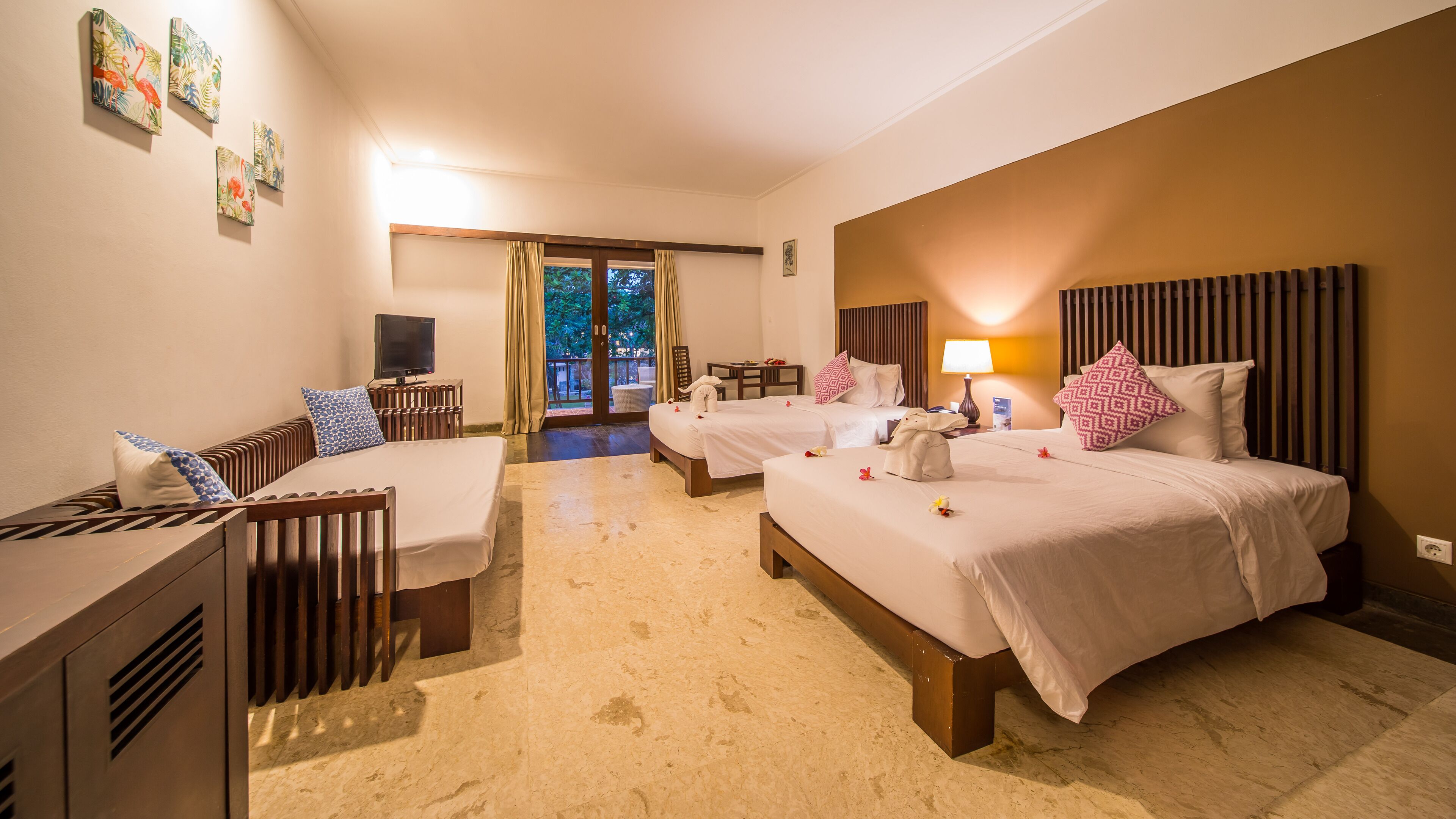 A hotel room with two beds, a desk, a TV, and a balcony with a view.