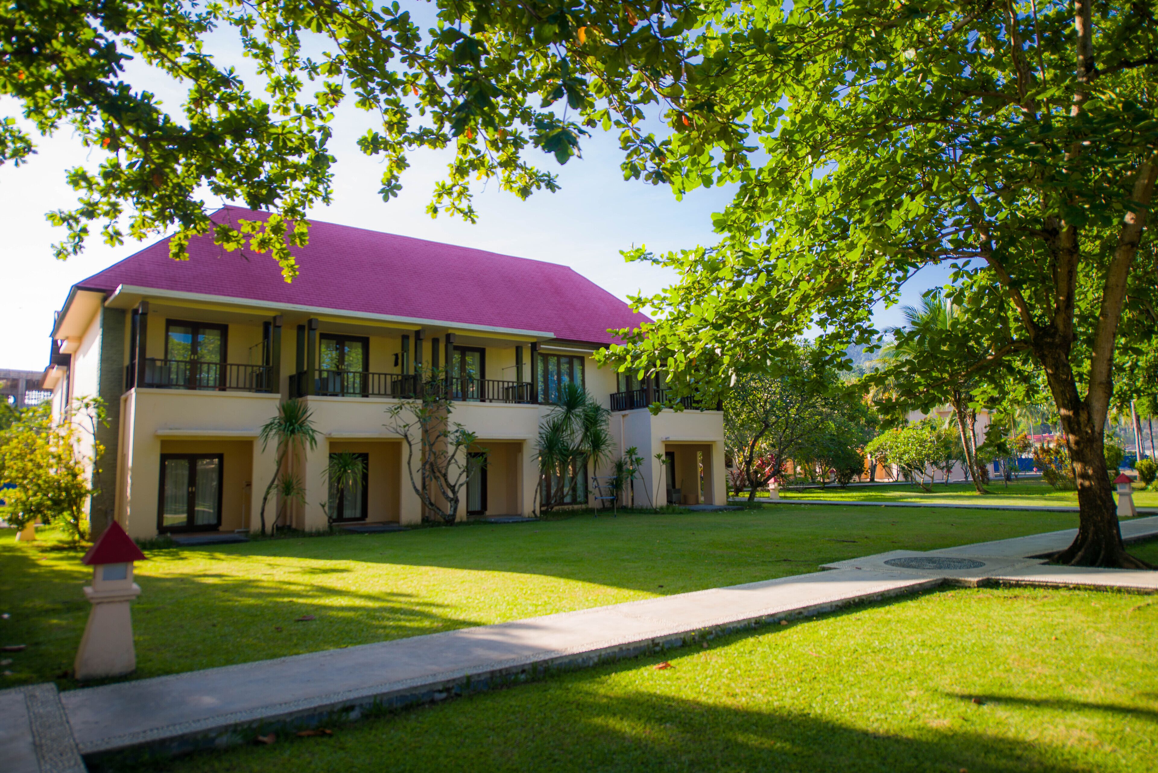 Un edificio de dos pisos con techo morado, un patio con césped y un árbol en primer plano.